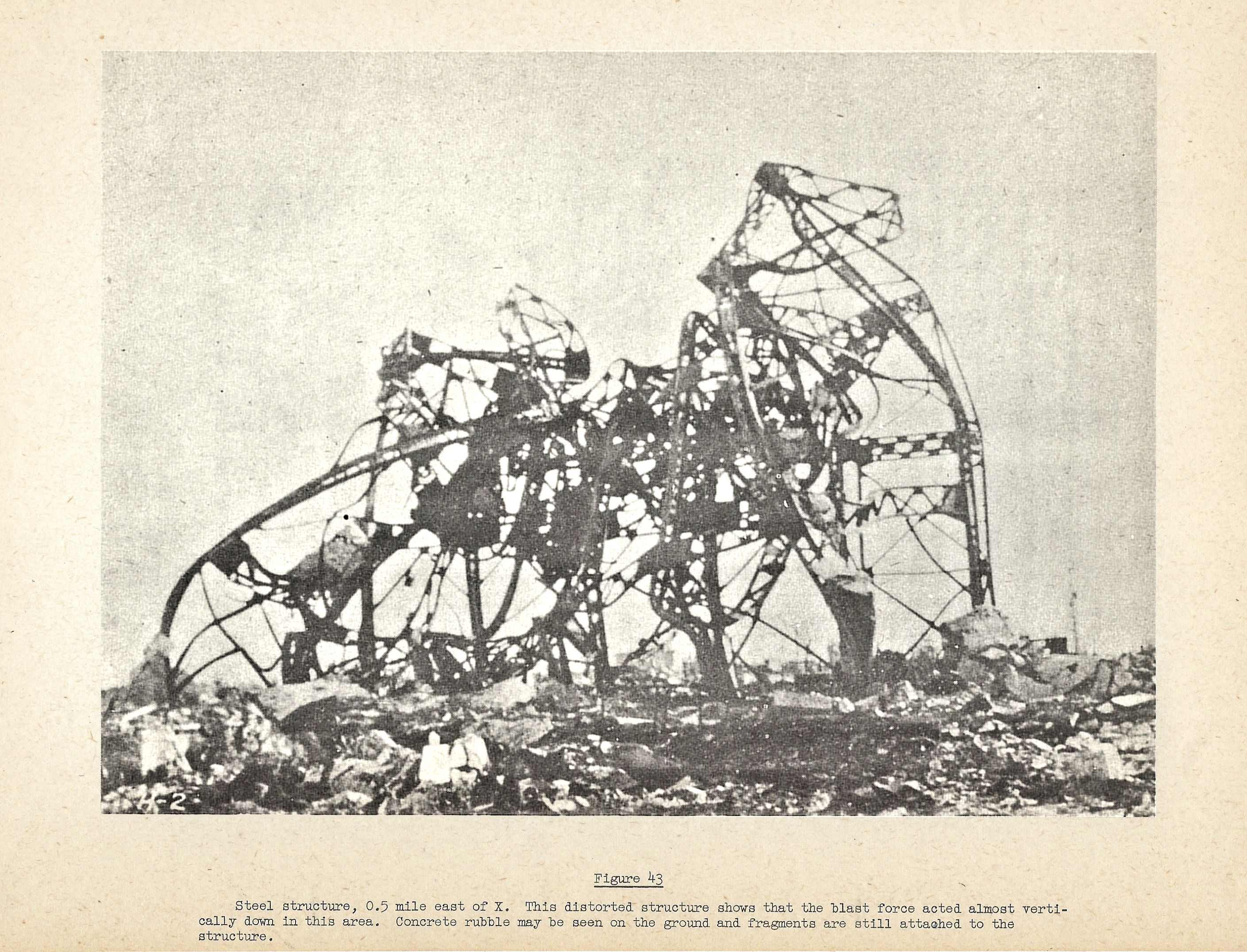 Steel Structure, 0.5 mile east of X. This distorted structure shows that the blast force acted almost vertically down in this area. Concrete rubble may be seen on the ground and fragments are still attached to the structure.